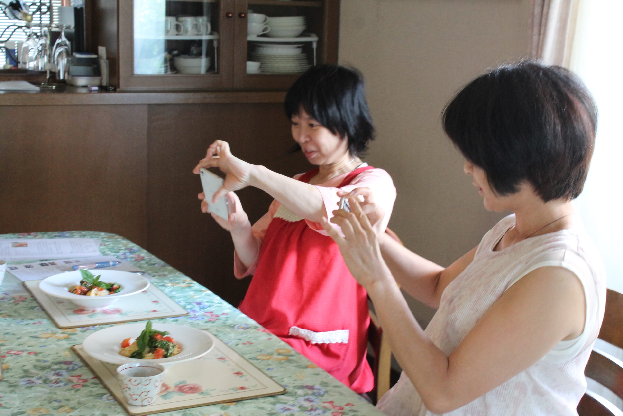 「生徒さんの笑顔が、何よりのご褒美」をイメージさせる、「登志子のキッチン」に参加して笑顔で料理の写真をスマホで撮影している生徒さんの画像